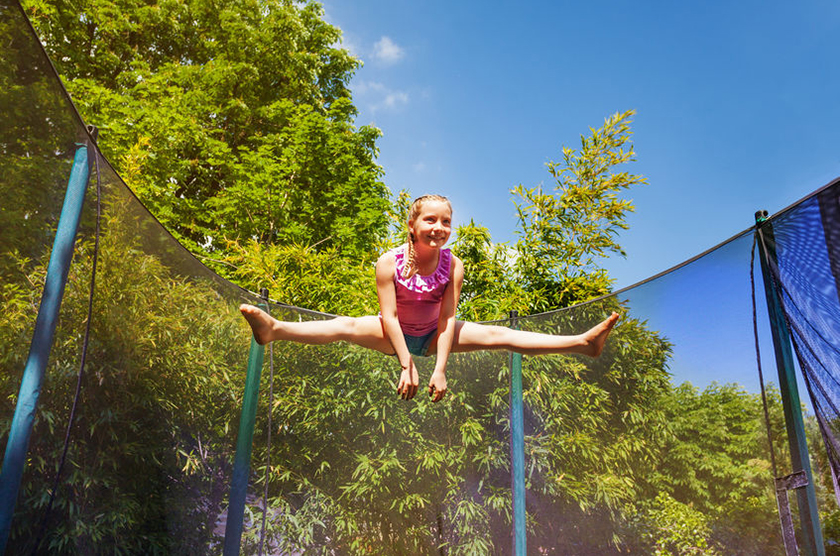 Low-angle portrait of preteen girl performing a split jump in the air, exercising on the trampoline outdoors